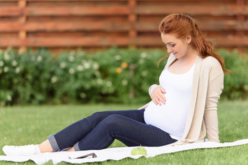 Obraz premium happy beautiful pregnant woman sitting on green lawn