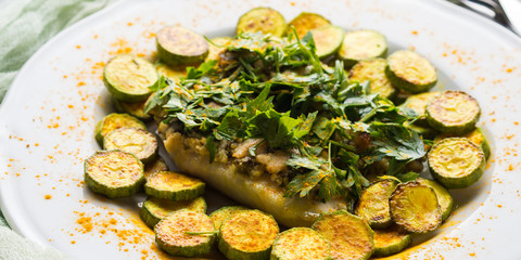 Baked Stock fish fillet with almond parsley topping and turmeric courgettes on white plate. Healthy diet dish