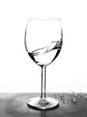 Half empty glass with water splashes in motion on white background.