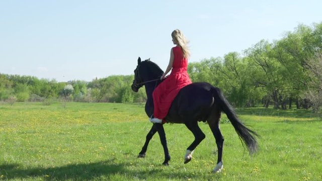 Young woman in red dress riding black horse bareback.