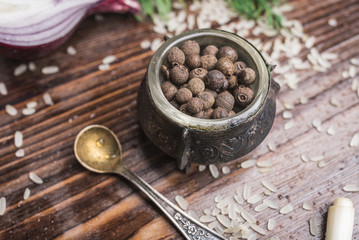 Black pepper in a vintage carved pepperbox, a small spoon, scattered rice on a dark brown wooden background