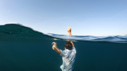young man sinking into the sea - obrazy, fototapety, plakaty