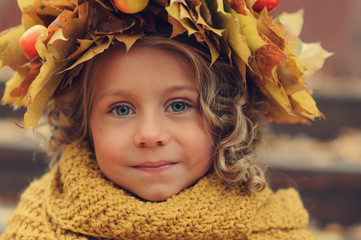 closeup autumn portrait of cute child girl in wreath made of dried leaves and orange knitted snood