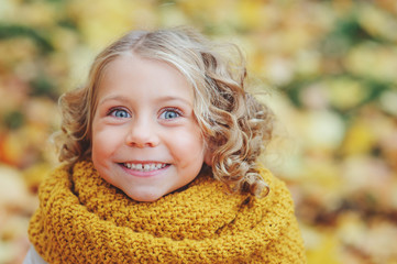 funny autumn portrait of happy toddler girl walking outdoor in stylish orange snood