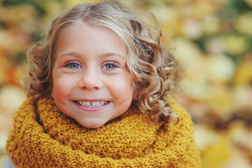 funny autumn portrait of happy toddler girl walking outdoor in stylish orange snood