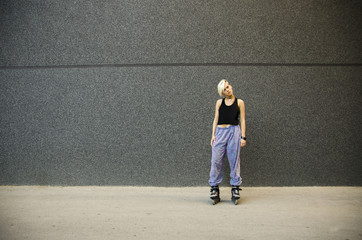 Young woman tilting hear head and standing wearing roller skates next to black modern  wall 
