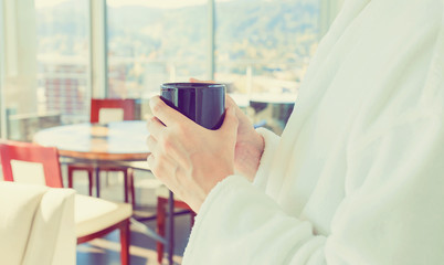 Young man in a bathrobe with a cup of coffee in a brightly lit modern interior room