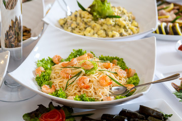 Pasta with shrimps in a white plate on a banquet table
