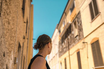 Rear view of brunette woman looking in street of old italian town. Sardinia. Italy.