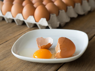 Chicken eggs cracked in white dish. The dish is placed on a wooden table. Front of many eggs.