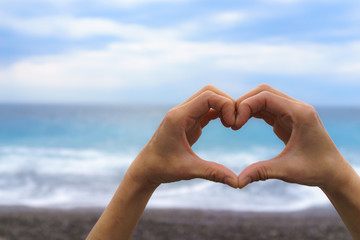 Close up of female hand making heart shape with blue sea and sky in the background