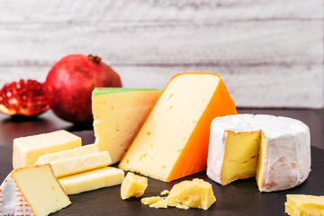 Cheese assortment and pomegranate on wooden background with copy space