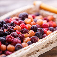 Close up image of wild berries in wicker basket on wooden table