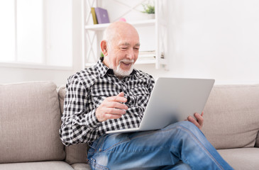 Naklejka premium Smiling senior man reading news on laptop