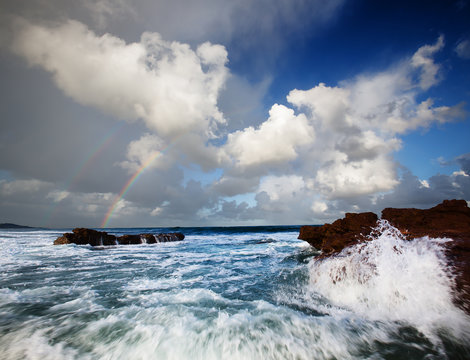 Vibrant seascape view at Scottburgh, South Africa, with a double rainbow and splashing water.