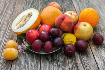 Melon, apples, plums, lemon, peaches, apricots and grapefruit on a wooden table.
