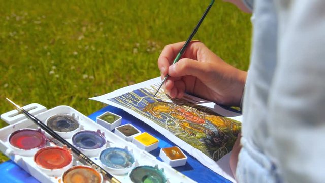 Detail of a woman painter/artist painting a picture using brush and watercolor, outdoors