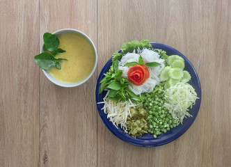 Thai rice noodle eaten with curry and veg. thai food (Thai language Kanom jeen) on blue dish and green bowl, All on brown wooden background / Selective focus and space for text..