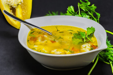 A delicious soup with vegetables and fish on a black background, very healthy healthy food in a white bowl.