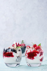 Traditional summer dessert Eton Mess. Broken meringue with whipped cream, berry jam, fresh blueberries and raspberries in two glasses, decorated with mint leaves over light blue concrete background.