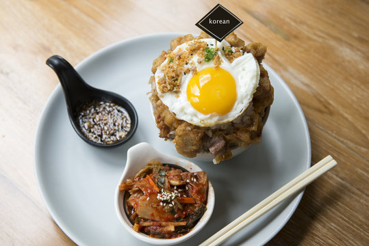 Fusion Korean food. Rice with pork and topping with egg. Side dishes are Kimchi and Korean radish preserved.