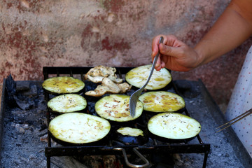 Unrecognizable person grilling chicken breasts and slices of eggplant. Selective focus. 
