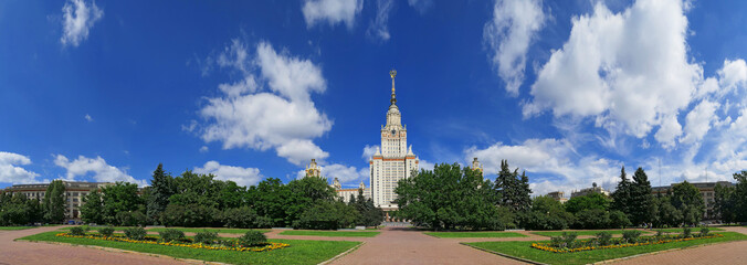 Wide angle frontal panoramic landscape view of light clouds over the sunny summer campus of...