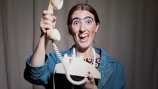 A funny ugly woman talking on a vintage rotary telephone and handing us the receiver. Comedy shot.
