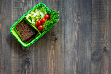 Heathy meal in office. Lunch box with tomato, salad and bread on dark wooden background top view copyspace