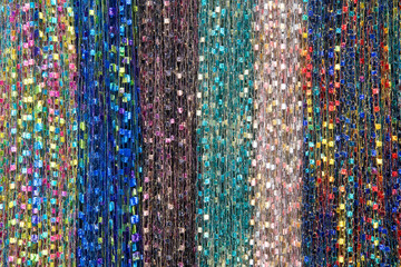 Background fabric strings creating scarfs, multiple colored scarves hanging in rows.. Blue, green, brown, rainbow pink, yellow. Hanging vertically