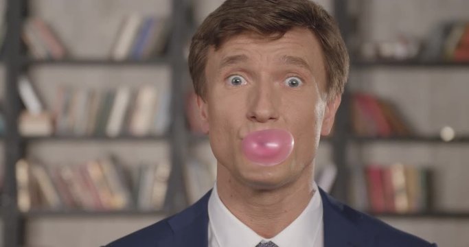 Slow Motion Portrait of Happy Successful Cheering Businessman Blowing Bubblegum Bubble. Having Fun Making Bubbles at Office. Businessman Series. 4K UHD 4096x2160.