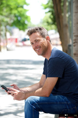 Portrait of happy man sitting on park bench with cellphone