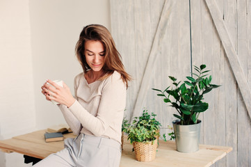 beautiful young feminine woman relaxing at home in lazy weekend morning with cup of coffee, wearing...