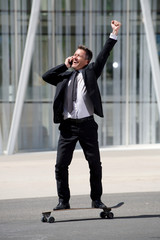 Full length fun businessman standing on skateboard on phone call