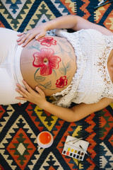 Pregnant belly mandala painting by an artist on young woman belly from above