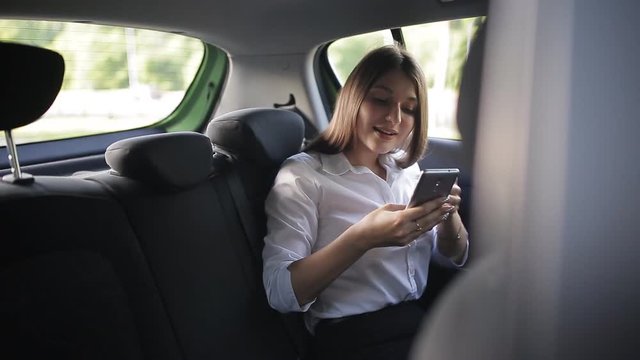 Closeup of businesswoman in car. Rear view of young handsome girl on the back seat of the car, talking on her phone suit waiting deal