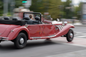 Old red speeding car riding on a street.