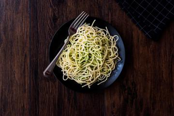 Spaghetti with pesto sauce on dark wooden surface.