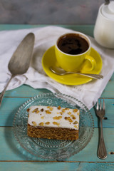 Carrot cake with coffee. Blue wooden table, cristal plate, yellow and orange cup.