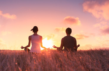 Man and woman meditating in a grass field at sunset.