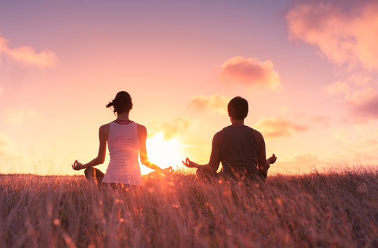Man and woman meditating in a grass field at sunset. 