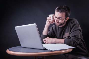 Young man enjoying his coffee and working on laptop, freelance writer or a blogger