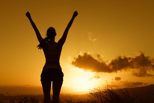 Happy victorious woman with her arms up facing the sunset. 
