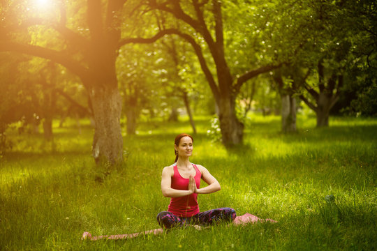 Woman sitting in yoga asana with crossed legs. Yoga in garden female doing Sukhasana yoga pose. Toned image.