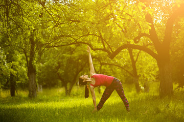 Girl doing yoga asana extended triangle. Yoga practicing outdoors, woman standing in Utthita...