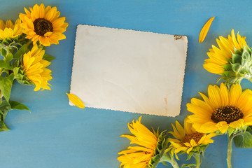 Sunflowers fresh flowers on blue wooden table background, copy space on empty paper note, top view