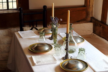 Pretty tudor dining table in a middle class medieval home, set with candles, glassware, cotton napkins and pewter plates