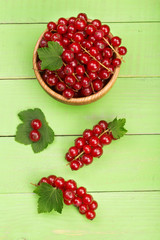 Red currant berries in a wooden bowl with leaf on the green wooden background. Top view