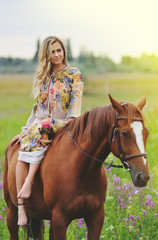 Fototapeta premium Young woman sits on a horse in a summer meadow