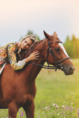 Young woman sits on a horse in a summer meadow